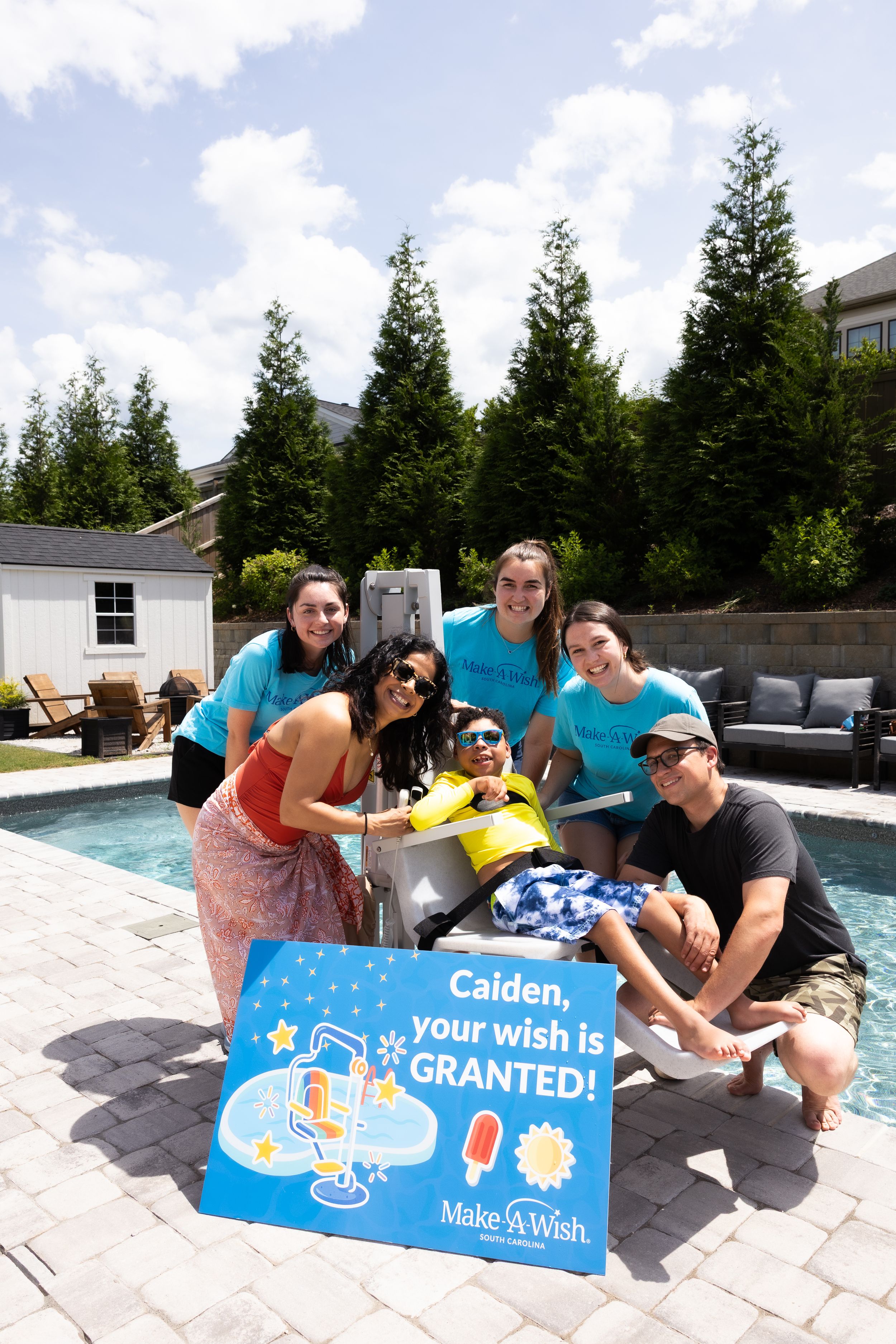 Group photo at a Make-A-Wish pool party celebration with blue sign in greenville, sc