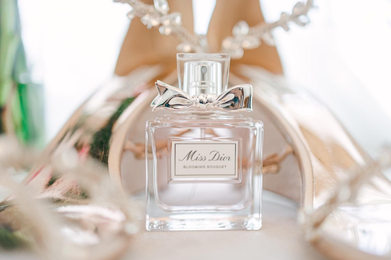 A bottle of Miss Dior perfume sits elegantly among soft white petals and delicate decor.