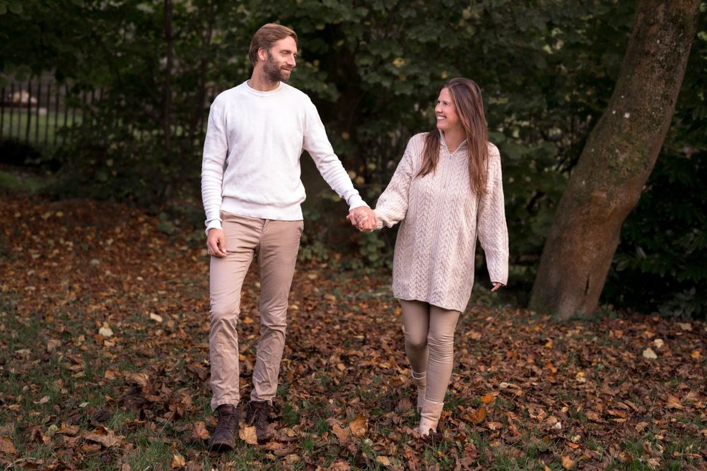 Familie spaziert gemeinsam in passenden Outfits in neutralen Tönen durch das Herbstlaub.