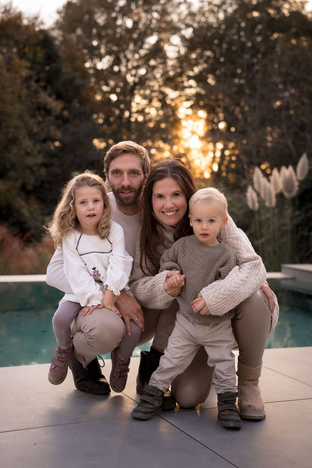 Eine vierköpfige Familie in passenden neutralen Outfits posiert gemeinsam am Pool bei Sonnenuntergang.