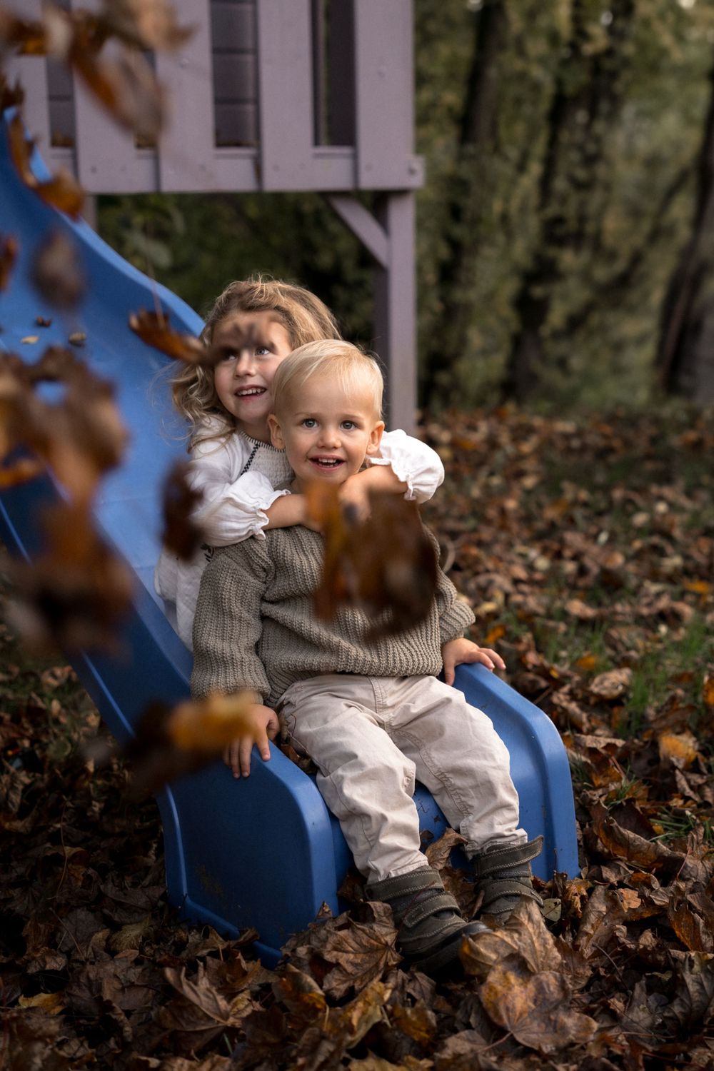 Kind sitzt auf blauer Spielplatzrutsche, umgeben von Herbstblättern.