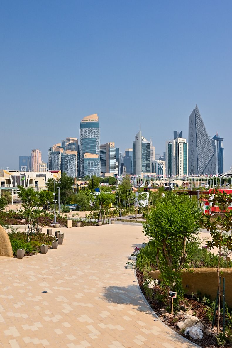 Modern skyline of Dubai with towering skyscrapers visible from a landscaped pathway. Things to do in Doha