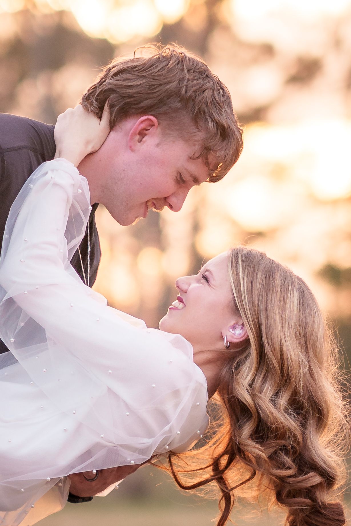 Romantic couple embracing in golden sunset light with dreamy bokeh background.