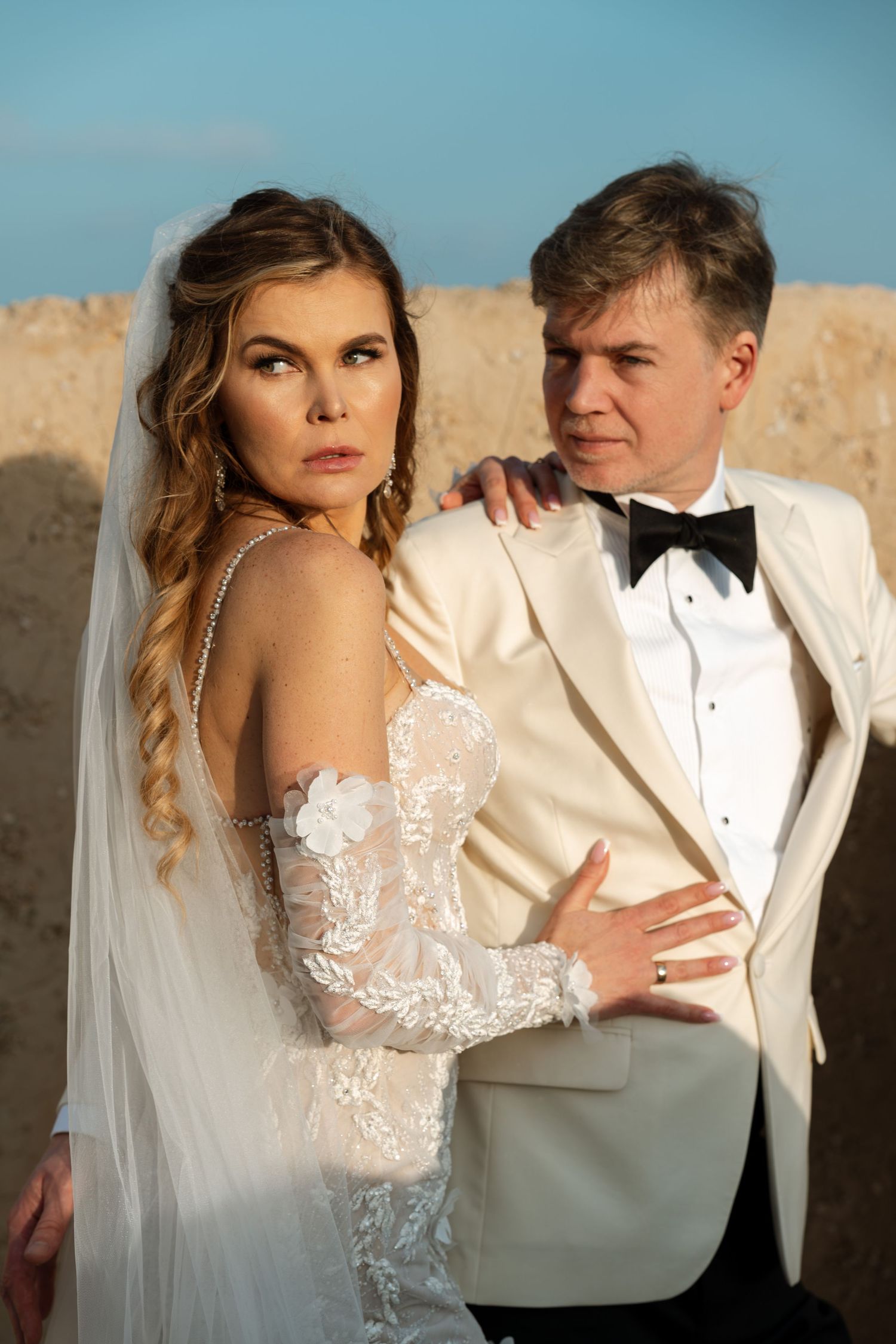 Elegancka panna młoda w białej sukni i pan młody w białym garniturze pozują na tle Zamku św. Barbary w Alicante