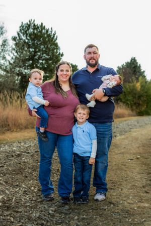 Family of five poses together on a dirt path with natural foliage in the background.