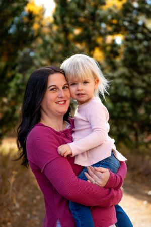Parent and young child in pink shirt share embrace outdoors during golden hour.