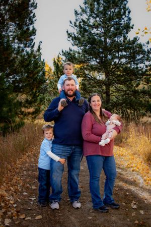 Family of five poses on a nature trail with pine trees and golden grass in the background.