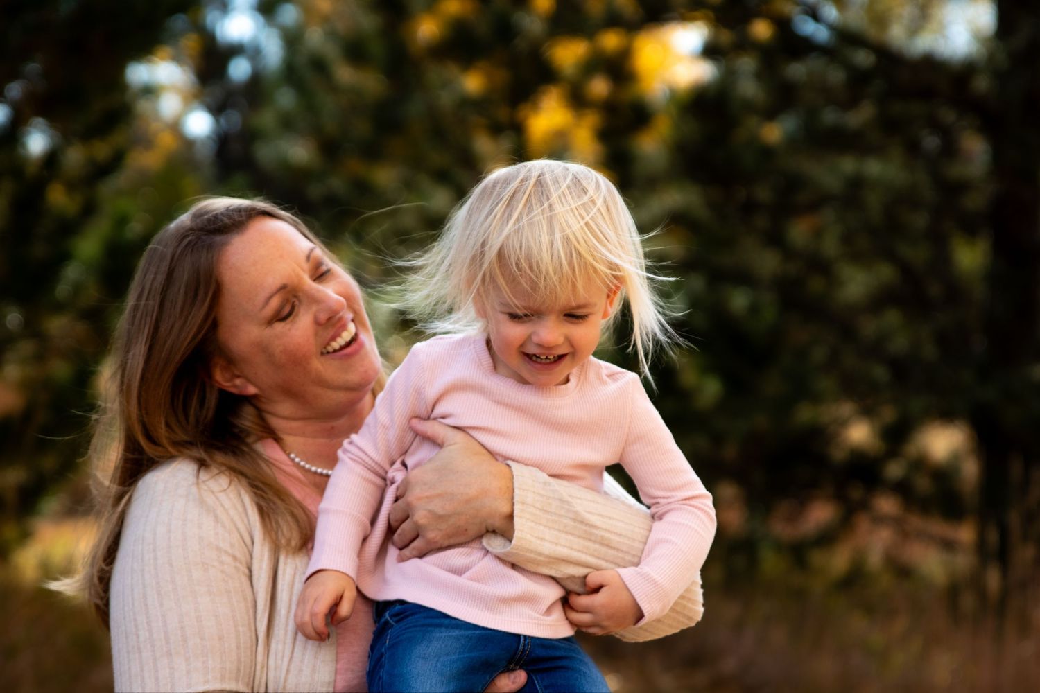 A parent and child share a joyful moment together in an outdoor autumn setting.