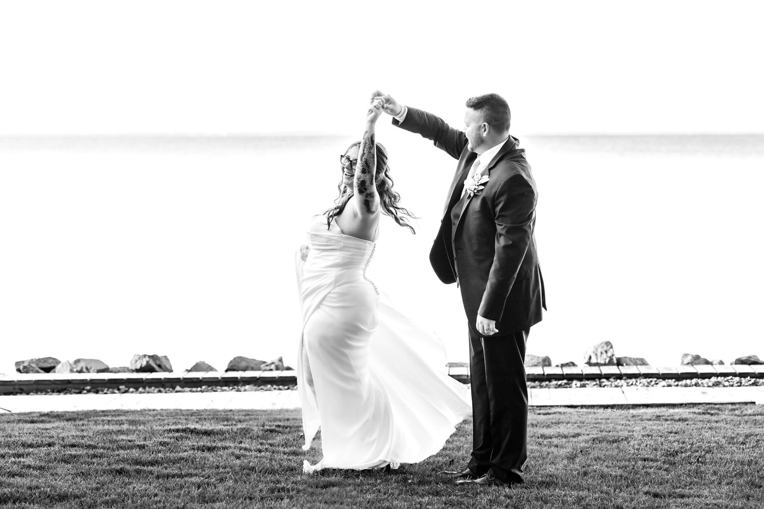 Black and white photo of a romantic dance pose on a grassy waterfront.