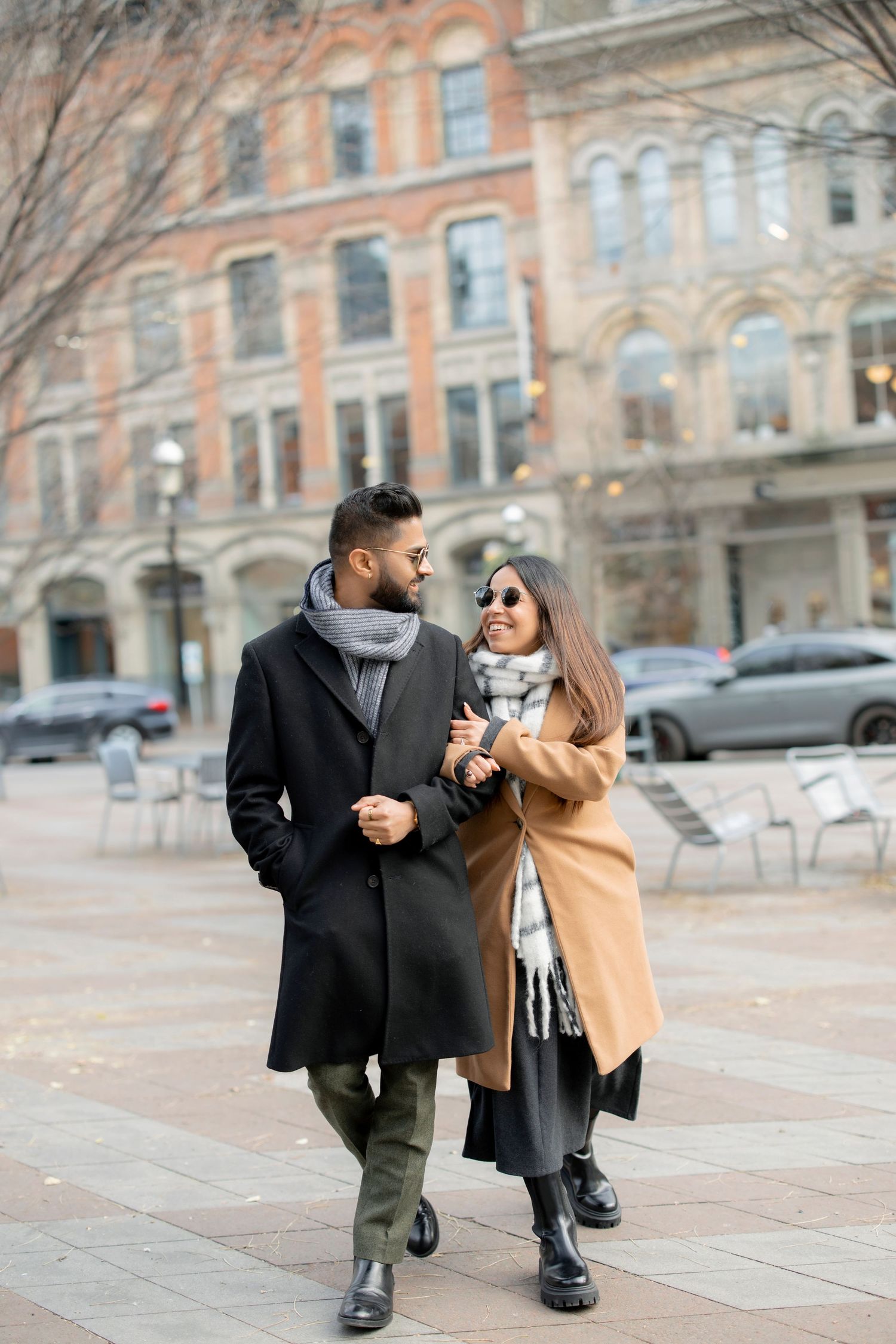 A couple strolling down a city street wearing winter coats on a cloudy day.