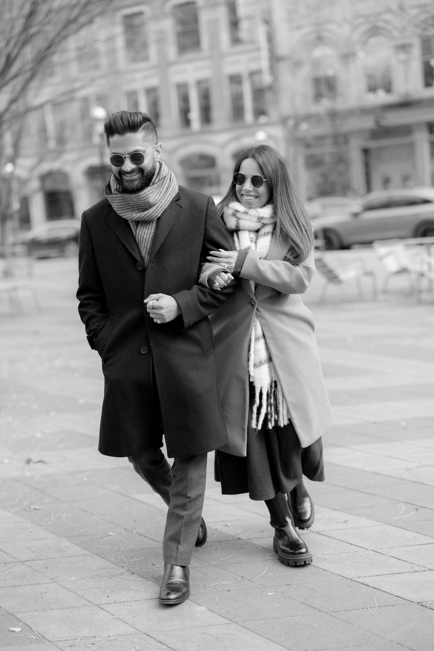 A fashionable couple in winter coats walking together on an urban sidewalk.