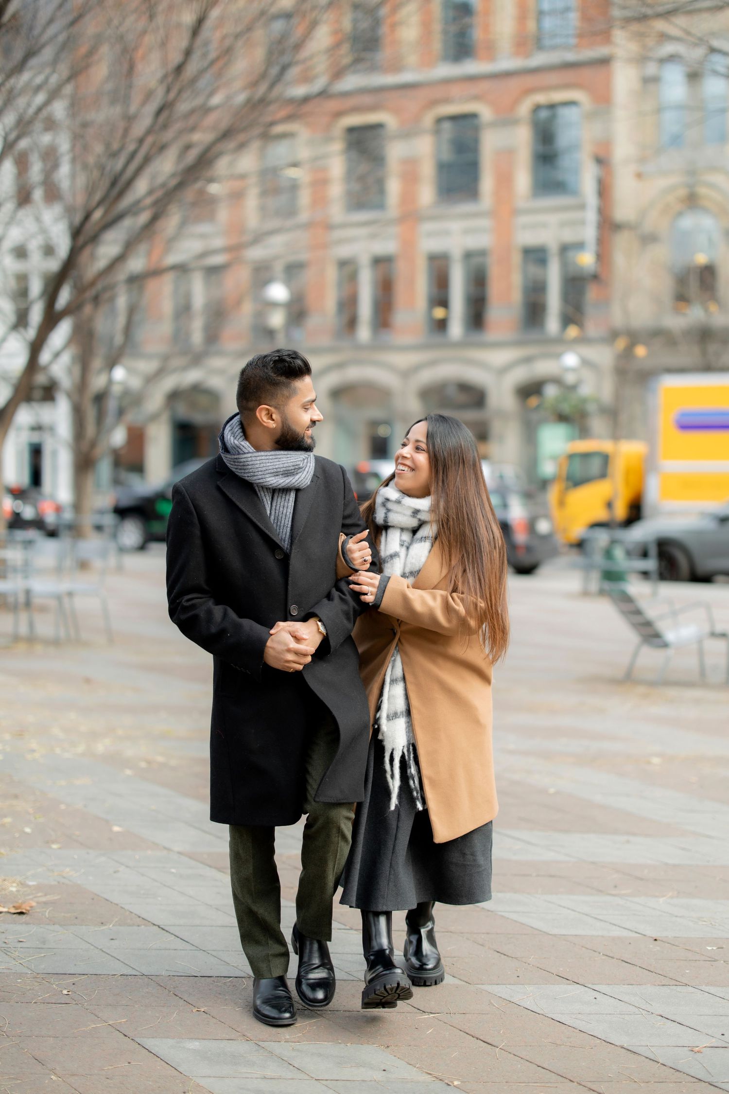 A couple sharing coffee and conversation while walking through a city plaza.