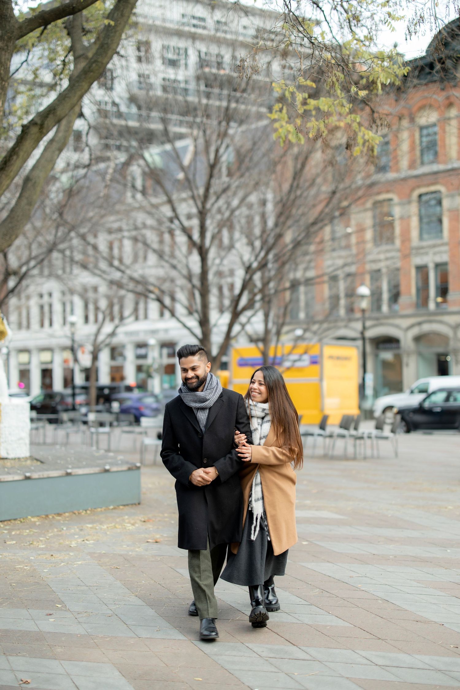 A couple taking a romantic stroll through a city square on a fall afternoon.