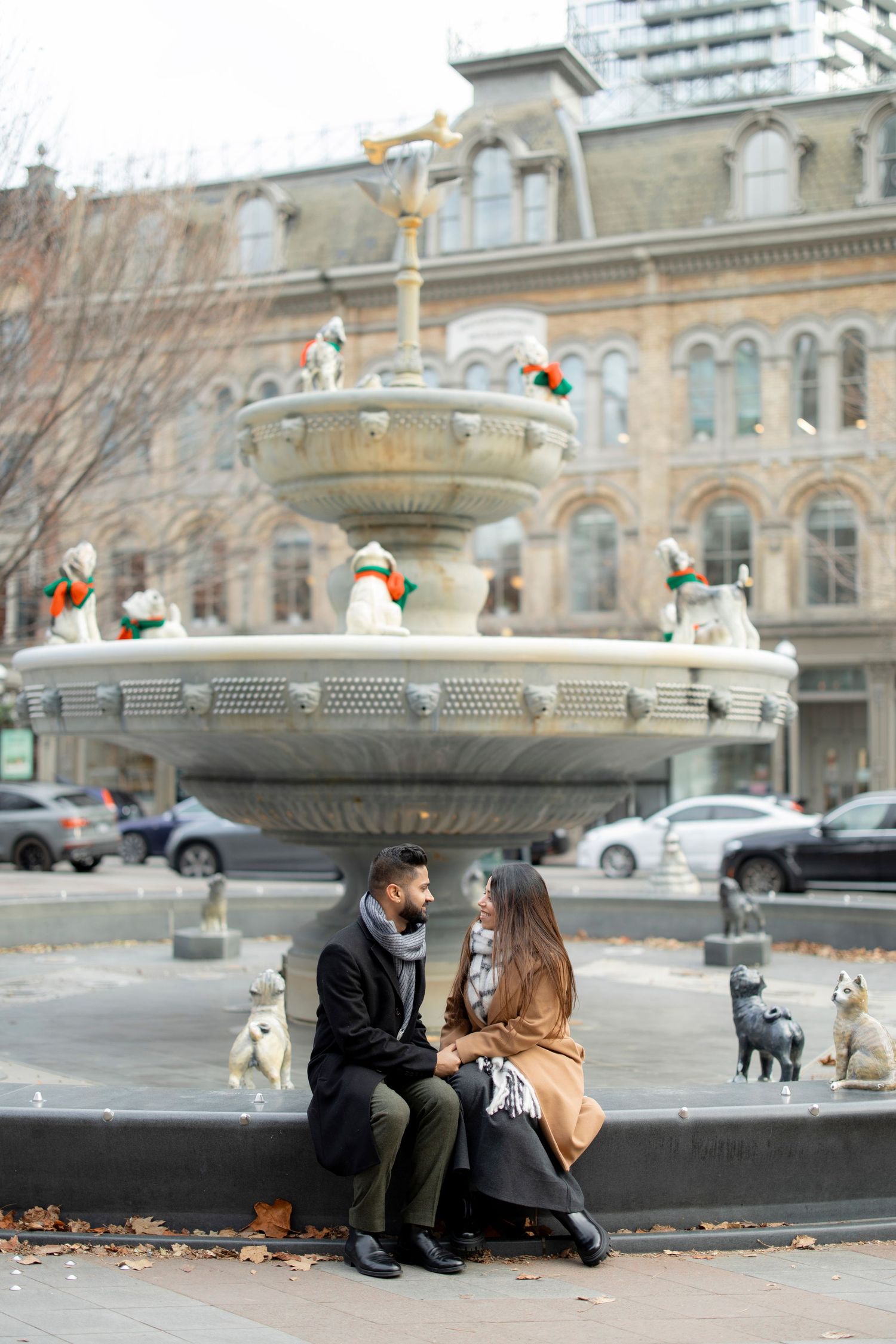 A romantic moment by an ornate fountain with cats wandering in an urban setting during autumn.