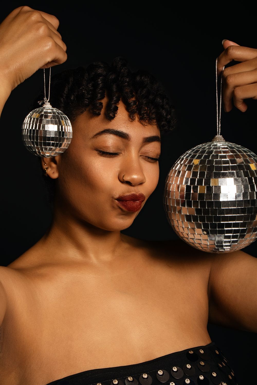 A dramatic portrait against black background featuring a disco ball and sequined outfit.
