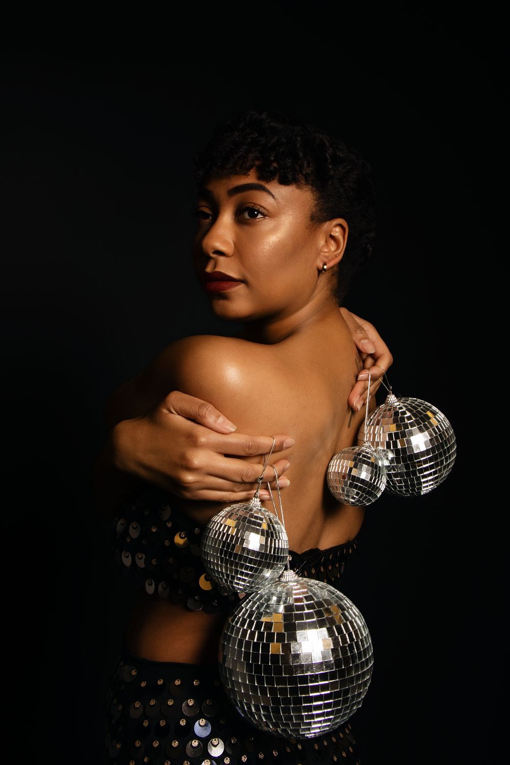 Elegant pose with disco ball and sequined dress in moody studio lighting.