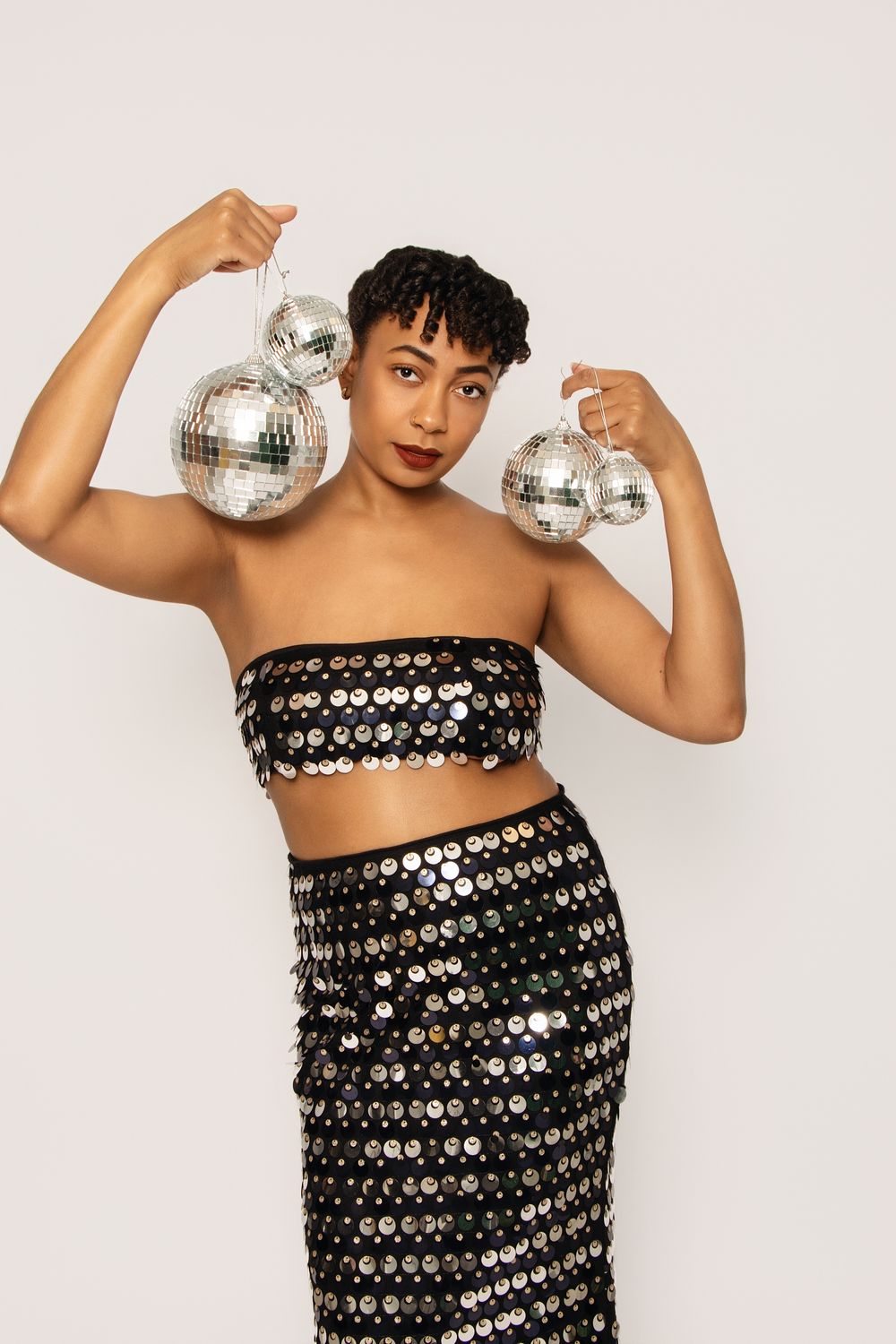 Dynamic poses with disco balls and sequined outfit against white backdrop.