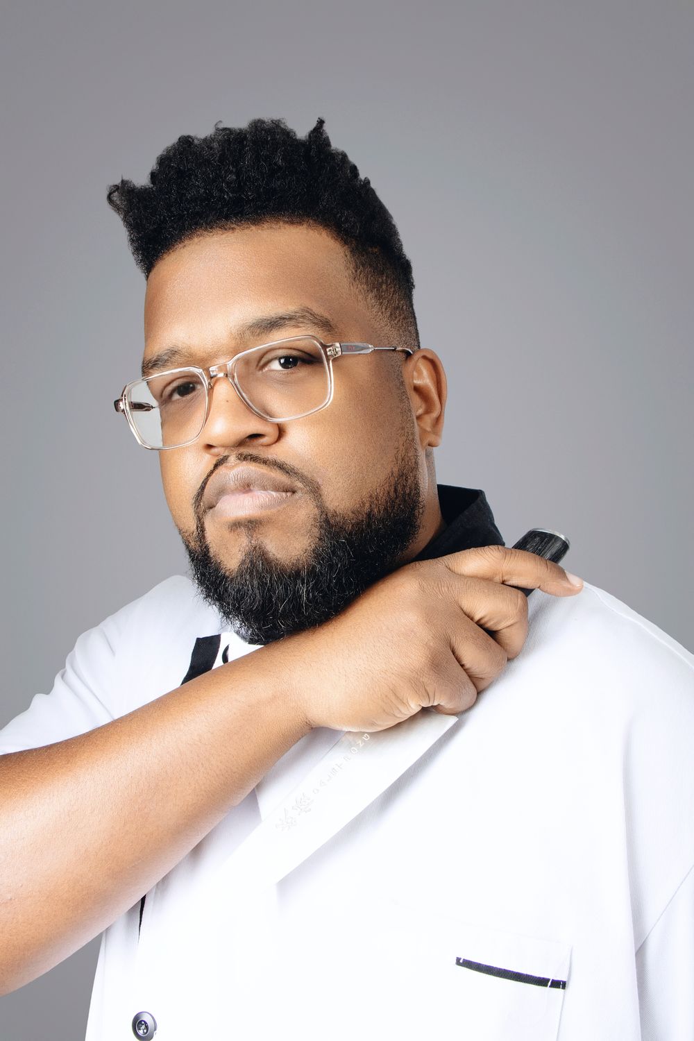 Portrait of person in white coat with glasses and beard adjusting collar.