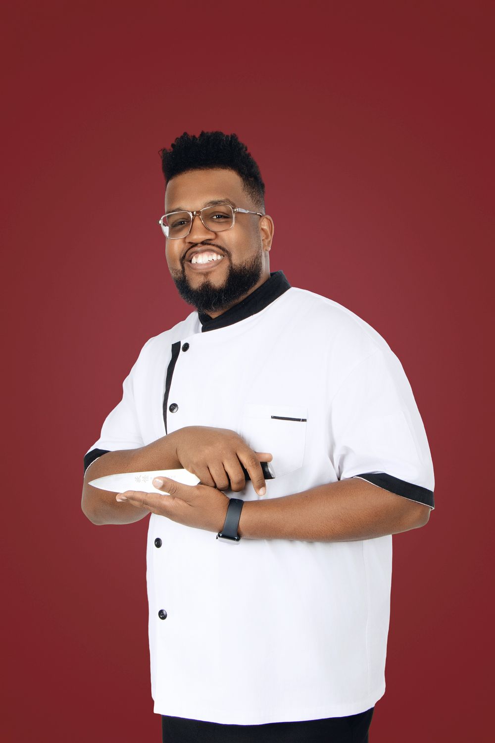 Person in white chef coat smiling against red background.