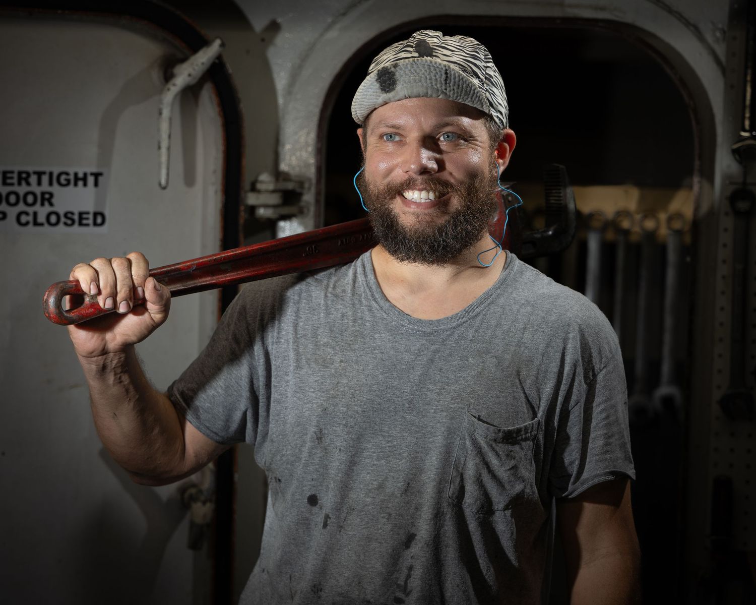 A person wearing a gray t-shirt and bandana holds a wooden bat over their shoulder in a dimly lit space.