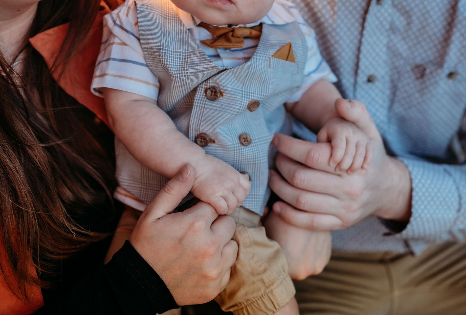 Close-up of hands holding small fingers in tender moment during family photoshoot.