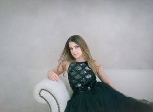 Elegant portrait in black floral dress seated on vintage chair.