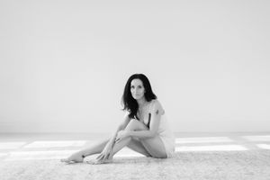 Black and white artistic portrait of a figure sitting on beach sand against a misty ocean backdrop.