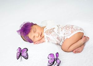 Baby sleeping peacefully in white lace wrap with purple floral headband and decorative purple butterflies nearby. #RoswellNM #Photographer