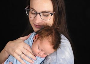 Parent gently holds sleeping baby in blue wrap against black background#Newbornphotographer #newbornpictures #babypictures #Tryingtoconceive