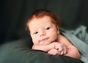 A newborn baby rests their chin on folded hands while lying on a dark green blanket #Newbornphotographer #newbornpictures #babypictures