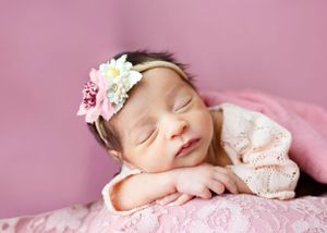 A sleeping newborn wearing a delicate floral headband rests peacefully on pink textured fabric #newbornphotographer #carlsbadNM #RosewellNM