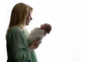 Mother holds a swaddled newborn baby against a white background. Carlsbad, Roswell NM, Artesia Newborn Photography. Backlit. Baby pictures