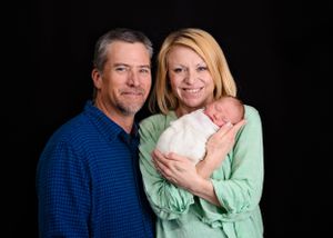 Mom and Dad blue and mint green shirts holding a small baby wrapped in white blanket. Carlsbad NM newborn picture. Newborn photographer.