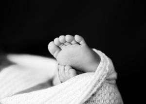 A black and white close-up photograph of a tiny baby foot wrapped in soft white knit fabric. #Details #Carlsbad #Roswell #NewMexico #Artesia