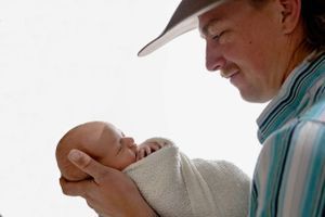 A tender moment captured as dad gazes adoringly at a newborn baby swaddled in white. #RoswellNM #newbornphotographer #artesiaNM #CarlsbadNM