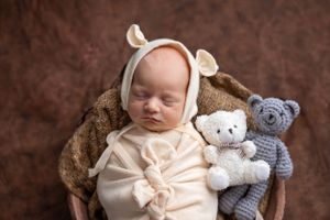 A peaceful sleeping newborn wearing a cream outfit lies in a cozy brown clay bowl against a brown backdrop. #newbornphotographer #carlsbadNM