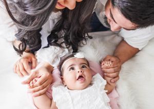 A baby looks up with wonder while laying on a soft white blanket being tenderly held from both sides. #NewbornPhotographer #NewMexico