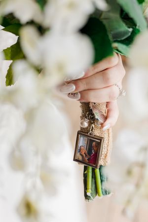 A series of small decorative photo frames being held against a backdrop of white flowers.