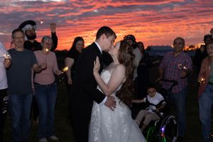 Silhouettes of people dancing outdoors against a vibrant orange and purple sunset sky.