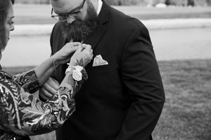 Black and white photo showing boutonniere being pinned to formal suit jacket.