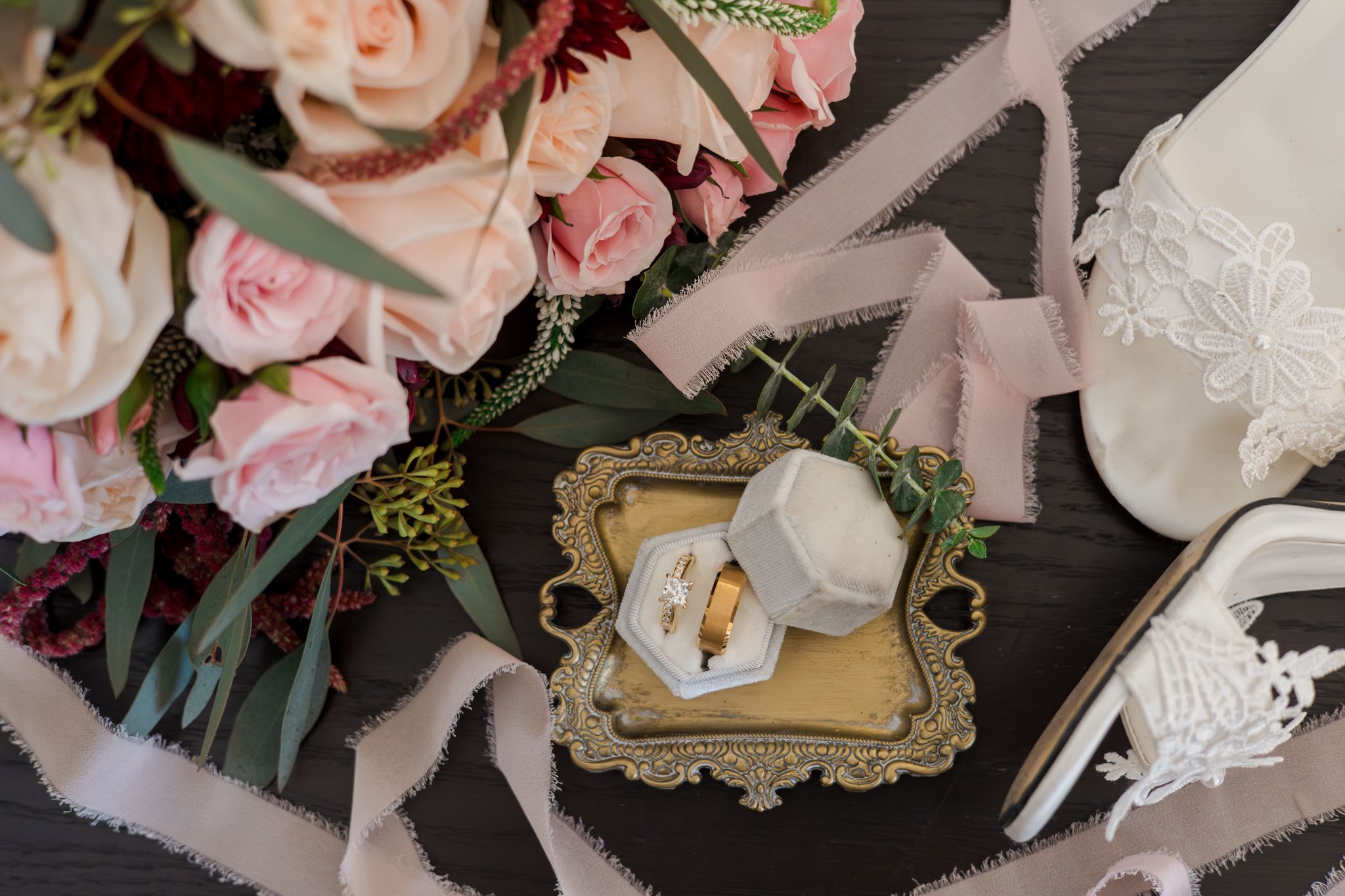 Wedding rings displayed in an ornate gold frame surrounded by pink roses and delicate floral arrangements.
