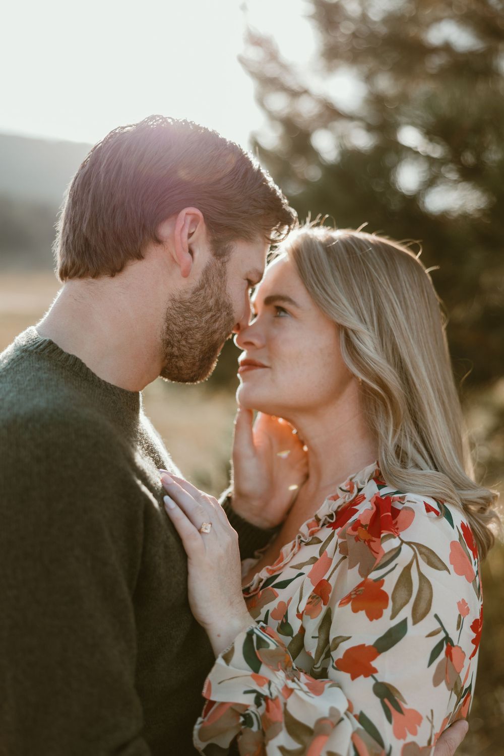 Intimate couple sharing tender moment in golden sunlight during outdoor portrait session.