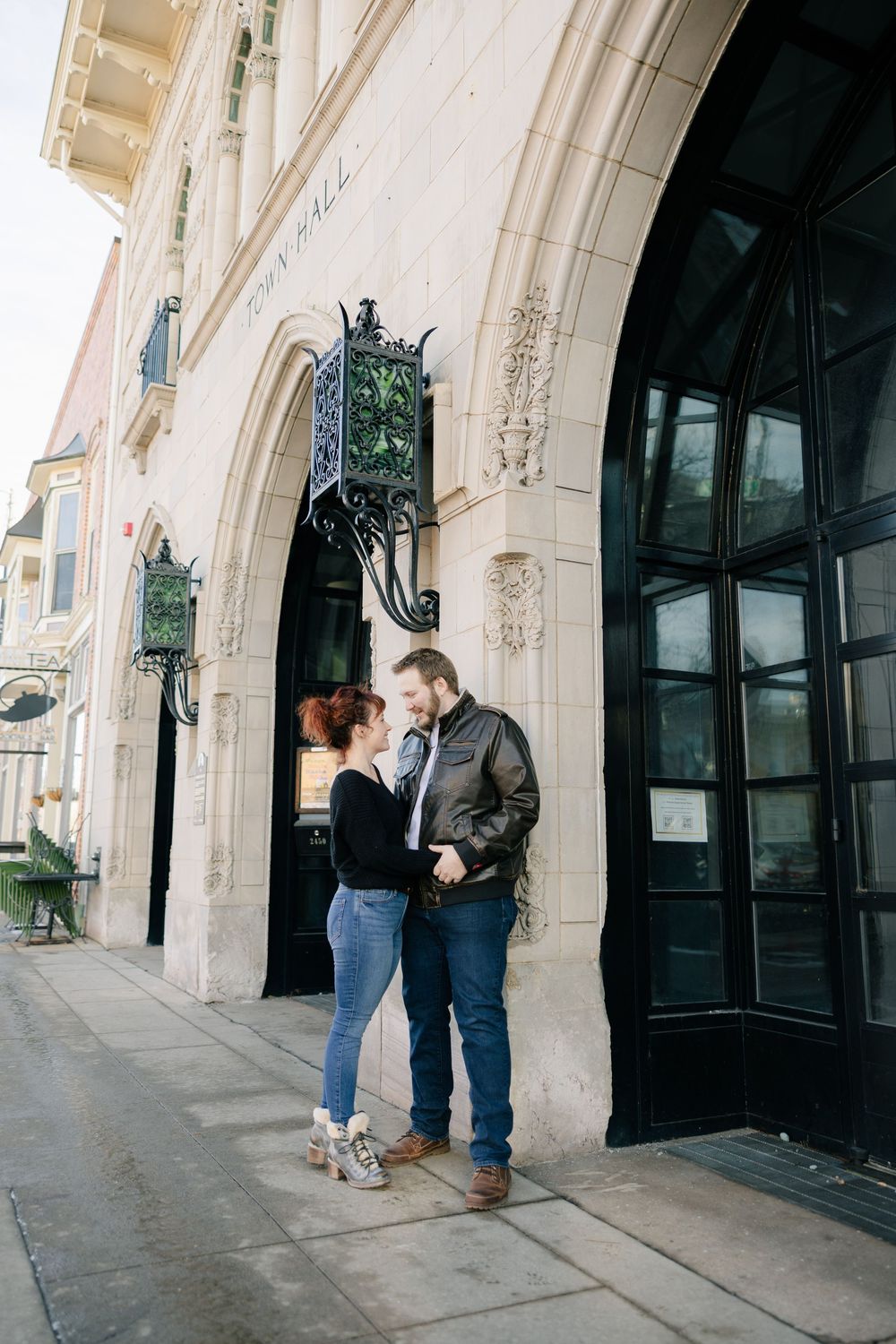 A couple shares a tender moment outside a building with ornate architecture.
