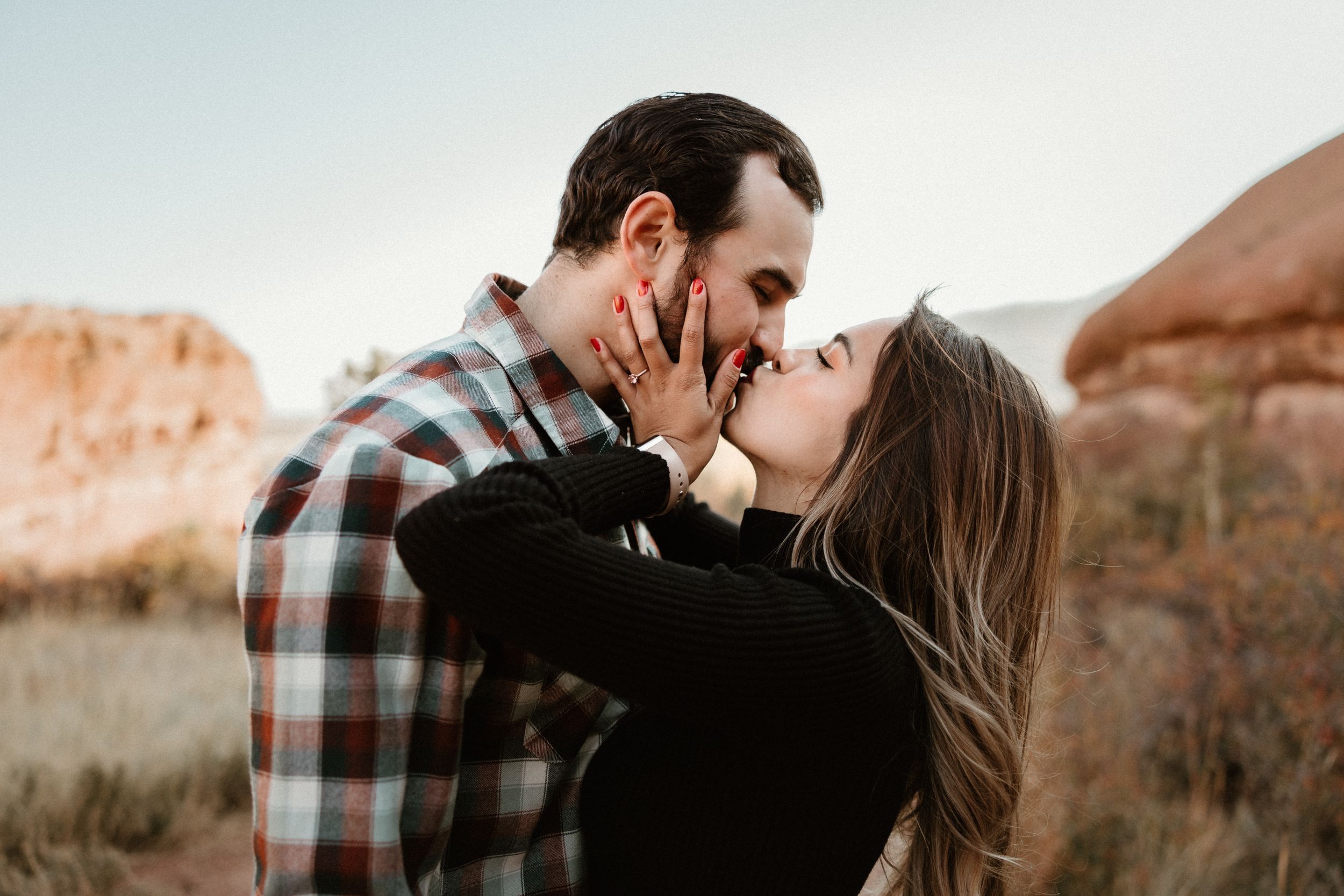 Intimate couple sharing passionate kiss against desert mountain backdrop at sunset.