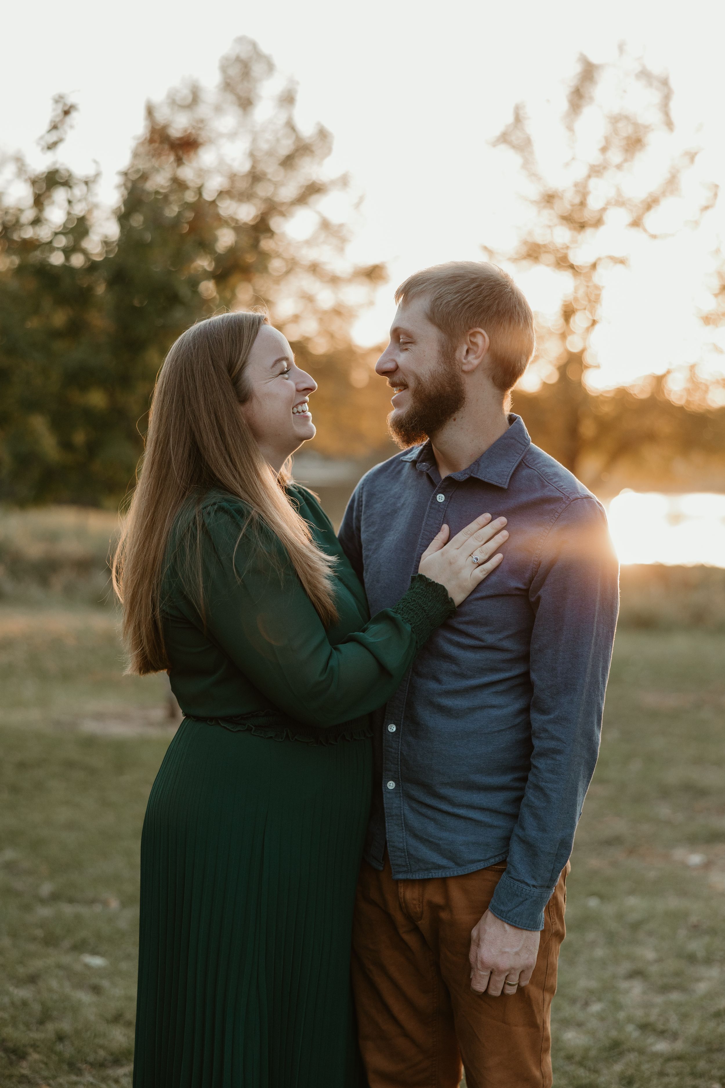A couple shares romantic moments at sunset in a grassy field while wearing casual clothes.