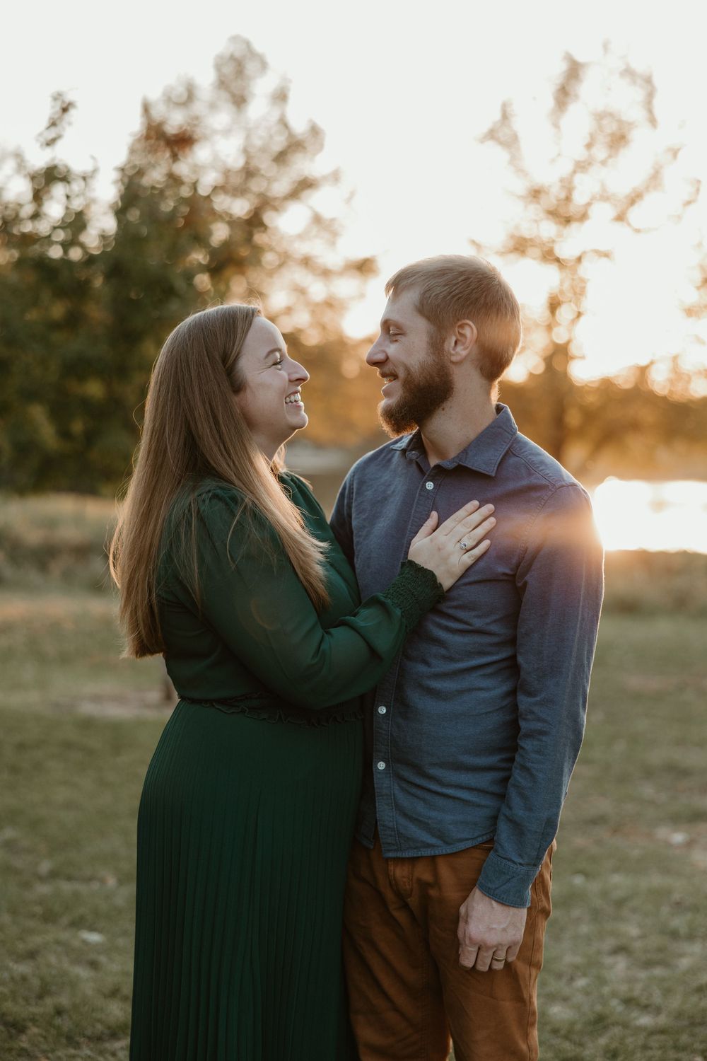 A couple shares romantic moments at sunset in a grassy field while wearing casual clothes.