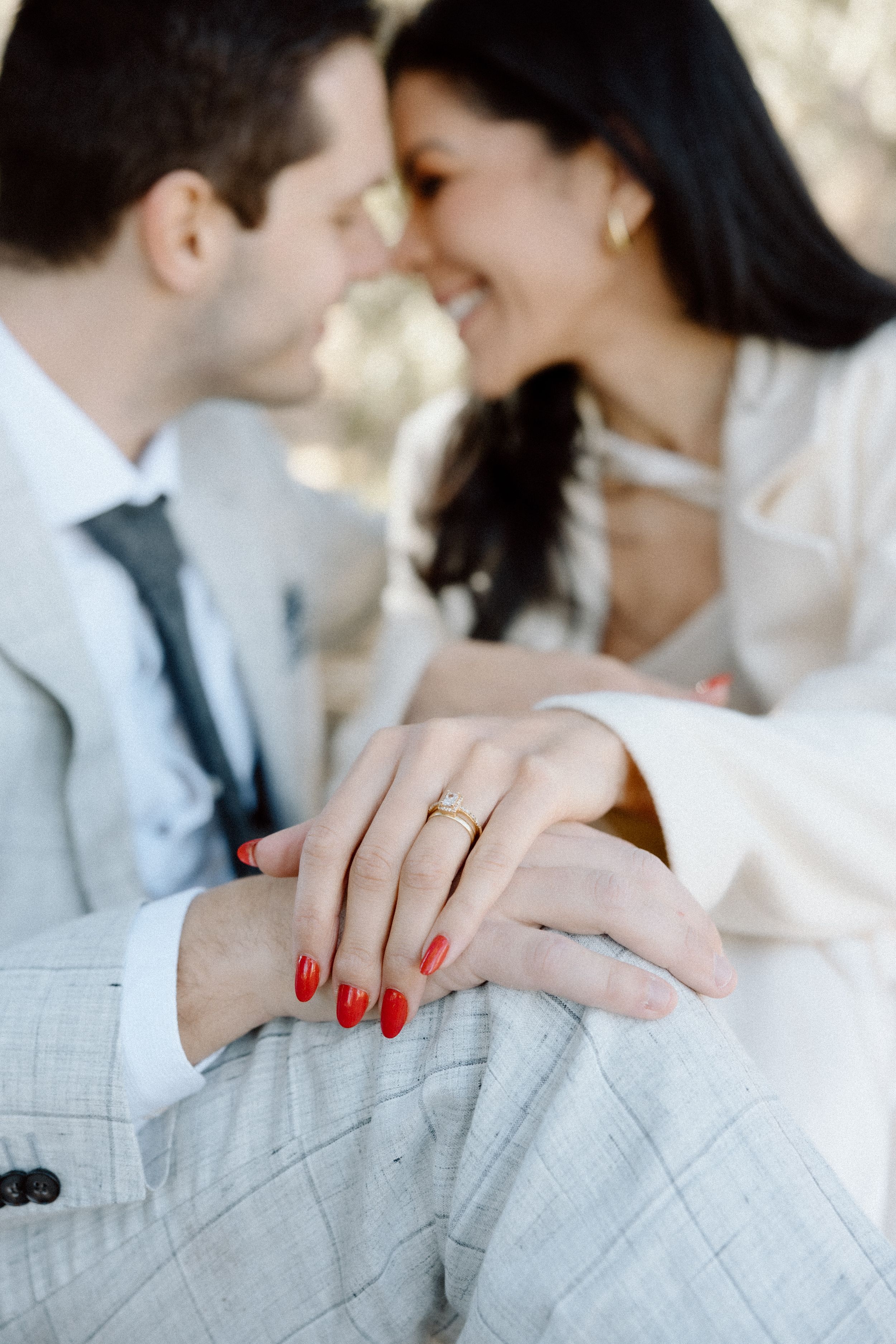 Close-up details of hands with red nail polish against light grey formal attire.