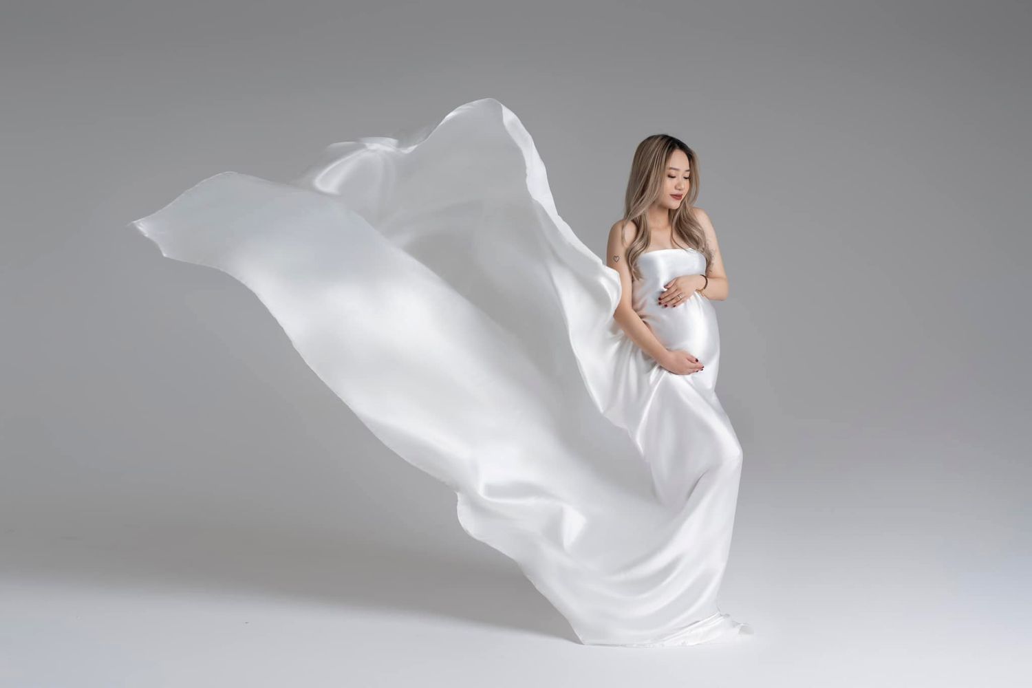 Maternity photo with flowing white fabric dramatically billowing around expectant mother.