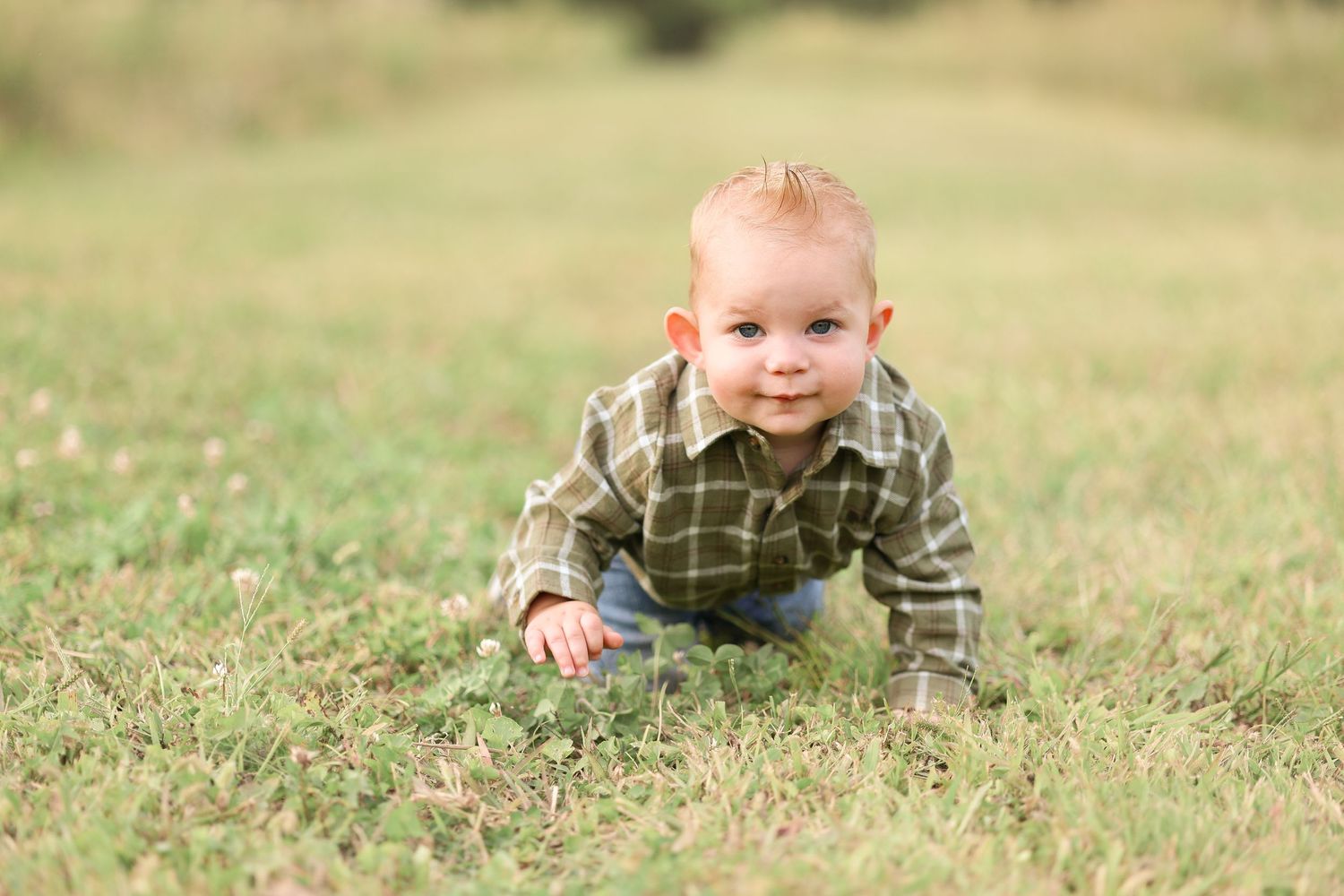 Young boy crawls through grass outdoors white smiling at the camera