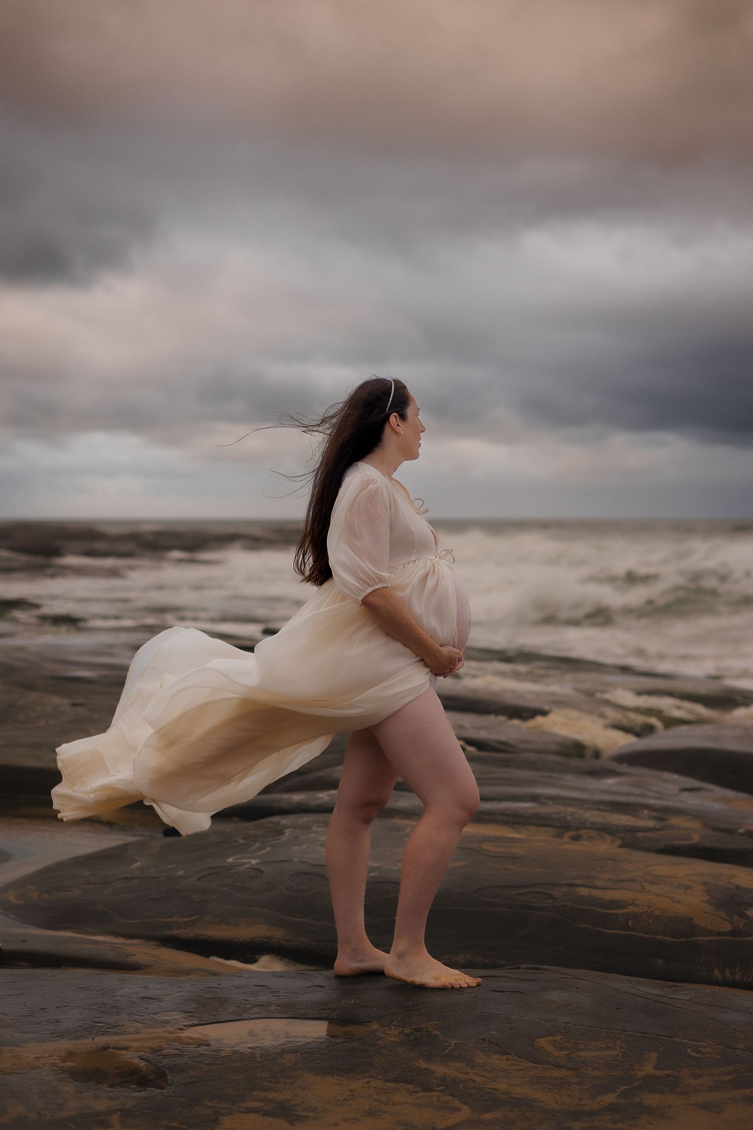 Authentic maternity portraits by the sea at Sunshine Coast, Australia, with a cinematic and moody atmosphere.